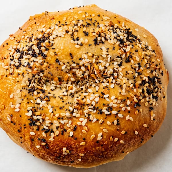Golden round bread roll topped with sesame, poppy, and assorted seeds on a white surface.