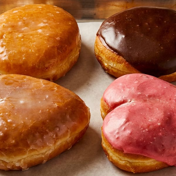 Four glazed pastries on a parchment-lined metal tray, featuring golden, chocolate, and pink icing.