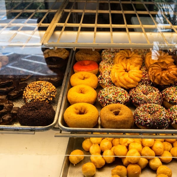 Bakery display case filled with assorted glazed, chocolate, sprinkled, and plain doughnuts.